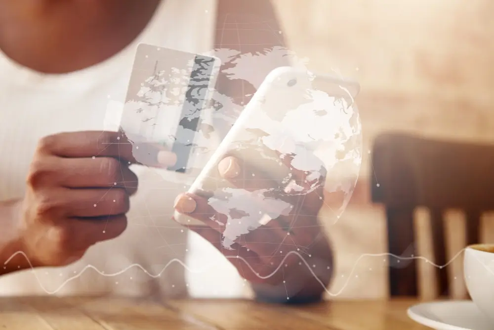 Pessoa segurando um cartão e um smartphone com mapa-múndi e elementos digitais sobrepostos, representando o uso de tecnologia e dados para reduzir custos e aumentar o controle do frete internacional na importação e exportação.